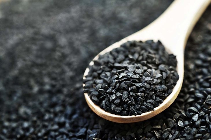 Black cumin (nigella sativa or kalonji) seeds in spoon on wooden background, selective focus, toned
