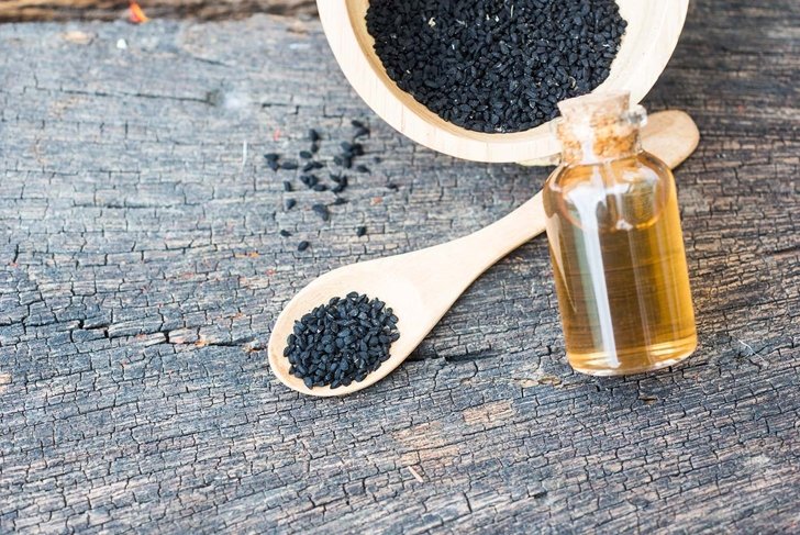 Selective focus Nigella sativa (Black cumin) on wooden spoon and essential oil. Real oil from nigella looks like dark honey. Herbal medicine.