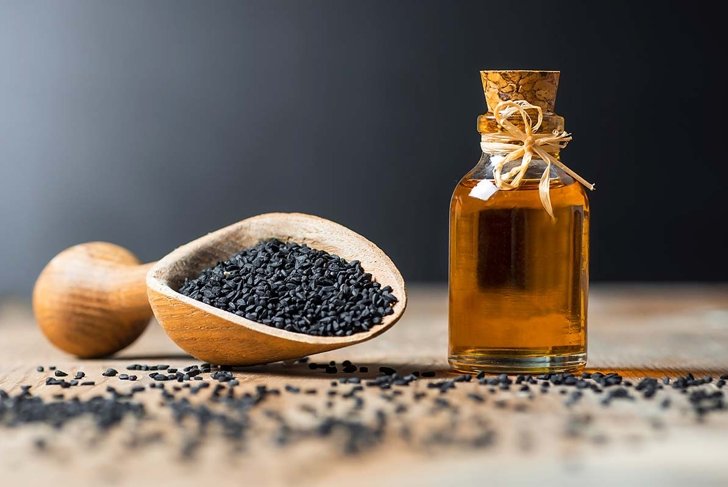 glass bottle of black cumin seeds essential oil , Nigella Sativa in spoon on wooden background. Organic herbal medicine for many diseases, black cumin