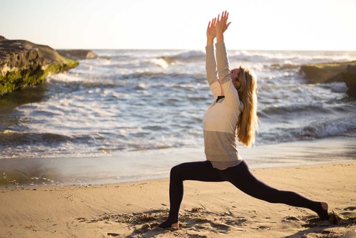 Blonde young woman doing yoga on the beach. Girl in black yoga pans, leggins and white sweater. San Diego, California