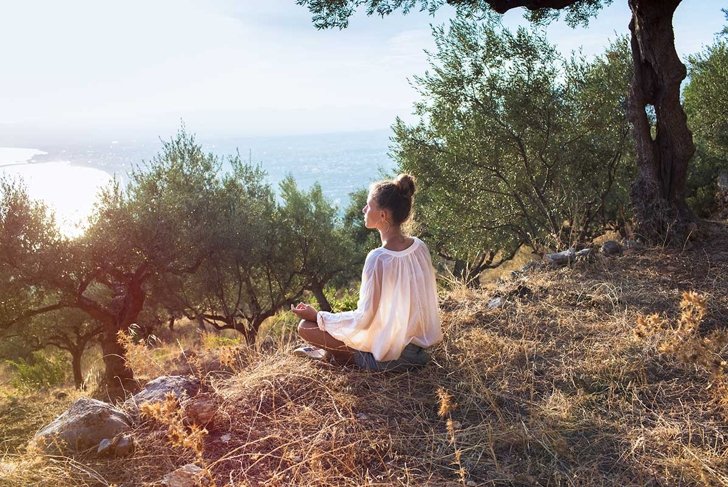 Yong women in olive field meditating toward the sea on sunset